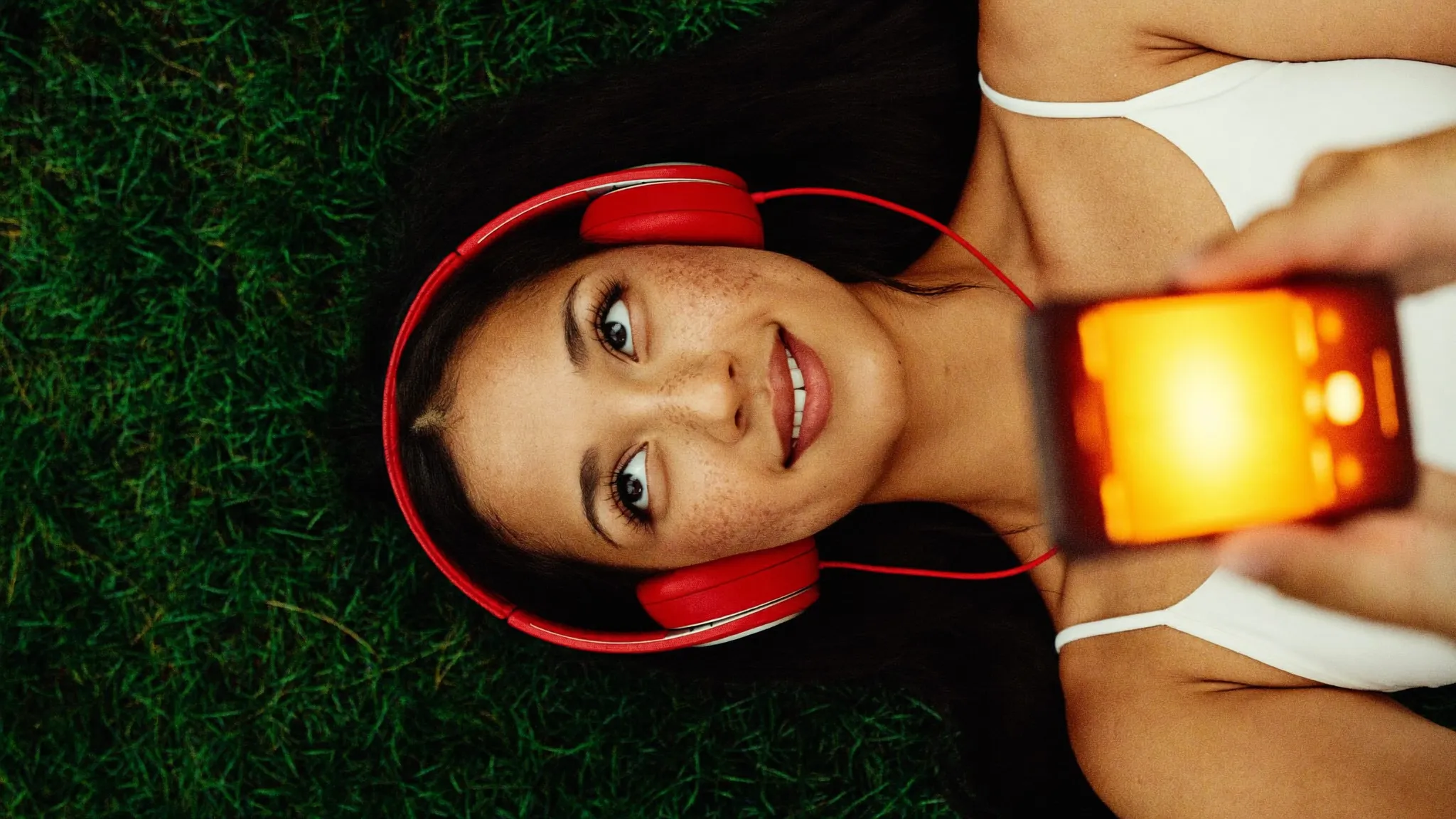 woman in grass with red headphones watching a glowing screen